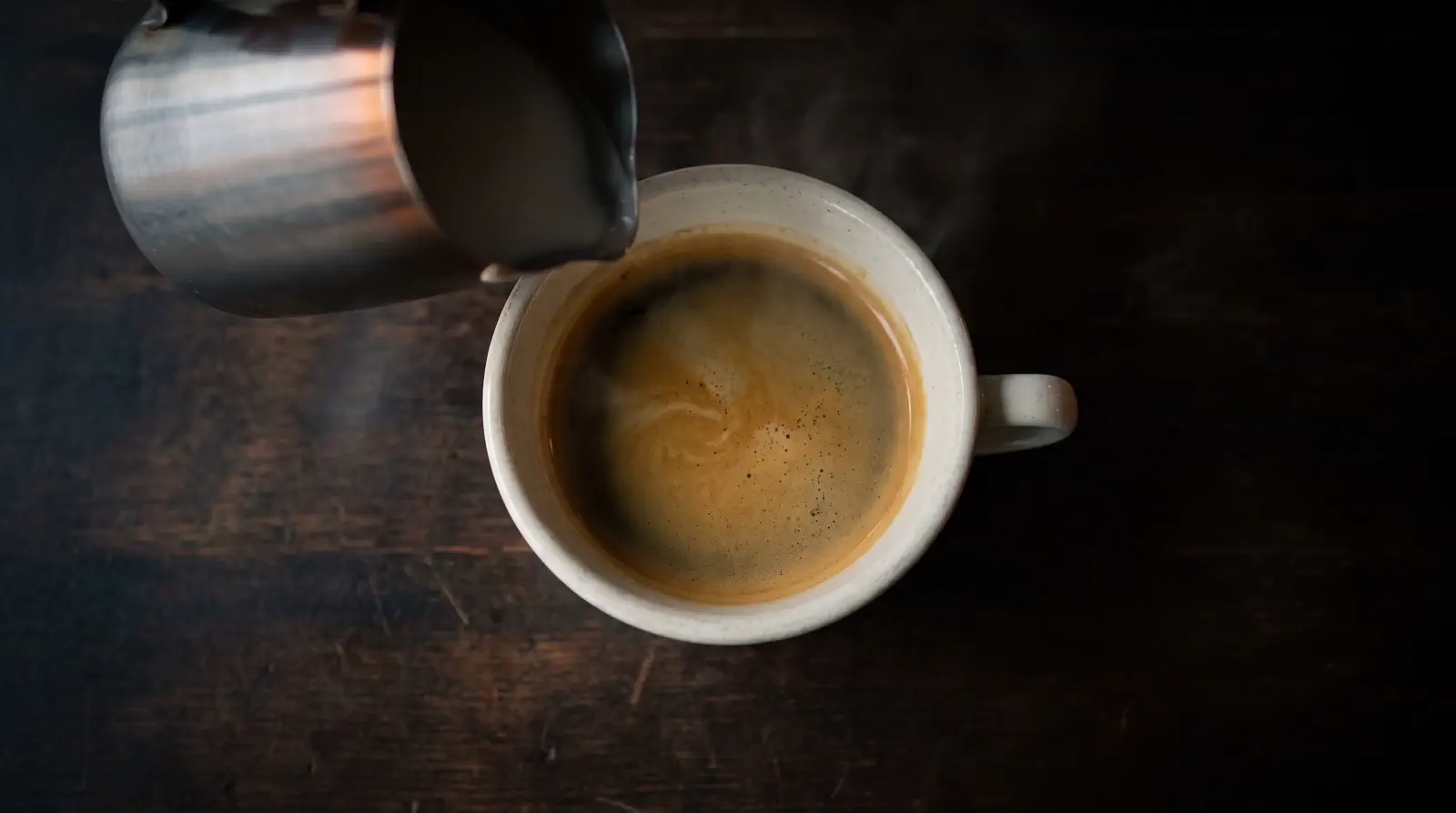 Milk being poured into a cup of espresso on a black slate table, seen from above