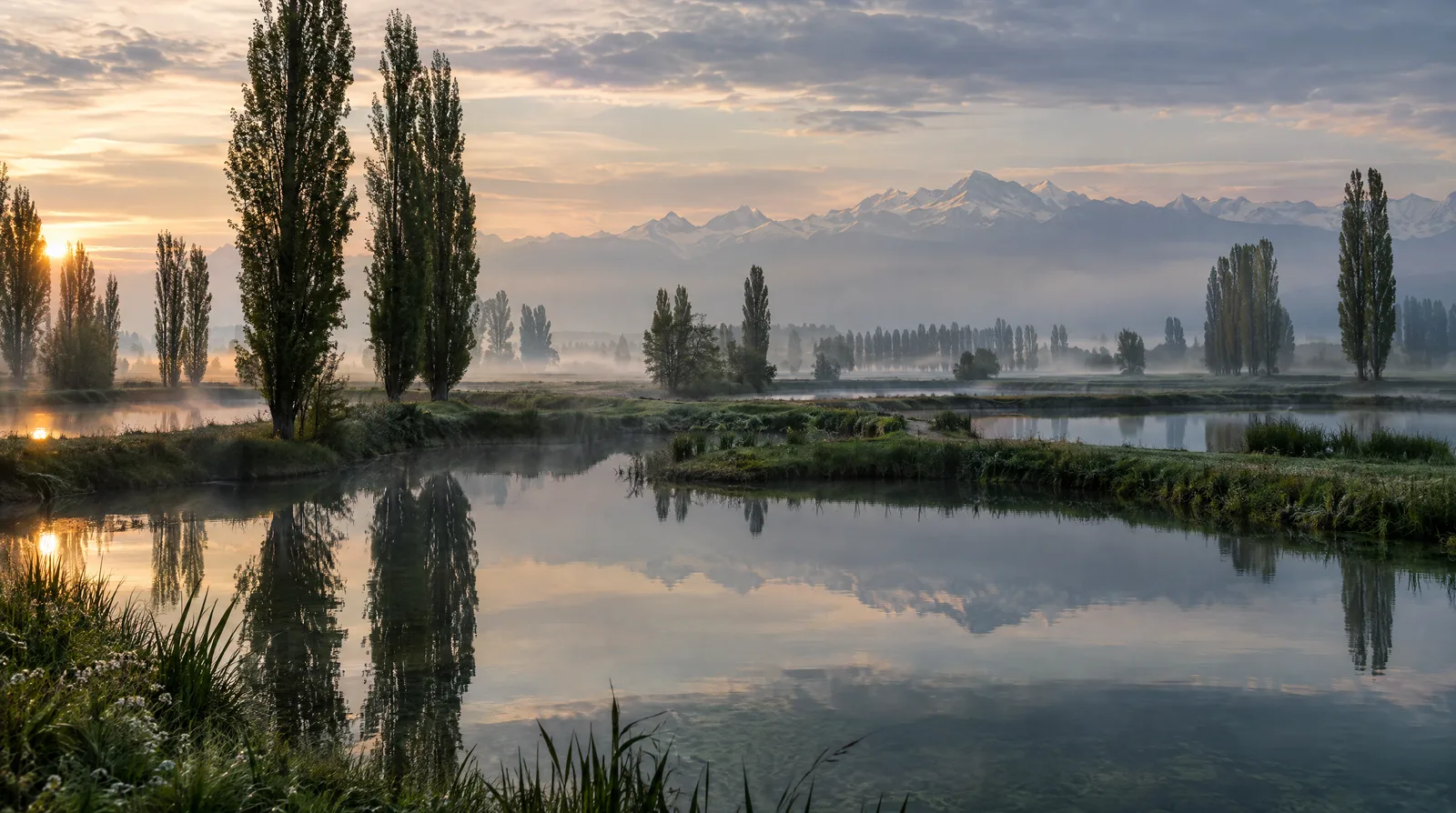 Calm spring-fed ponds on the Lombardy plain at misty dawn with the Alps on the horizon