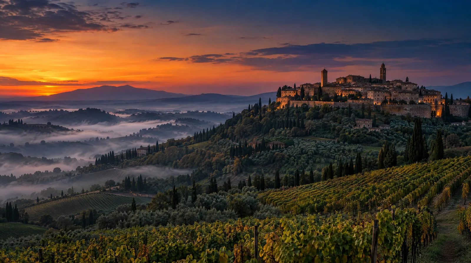 The hilltop town of Montalcino above vineyards and olive groves at dusk