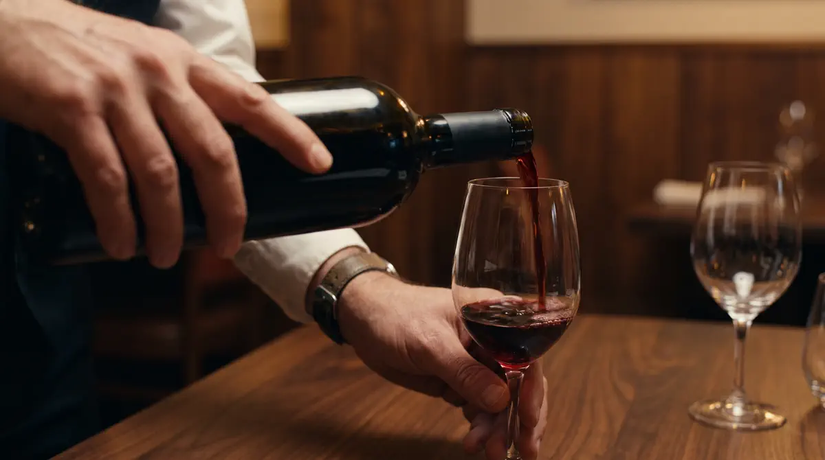 A sommelier pouring red wine into a crystal glass in a dark tasting room